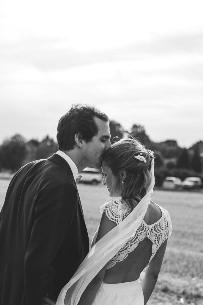 Une photo de couple de mariés en noir et blanc, le marié fait un bisous sur le front de la mariée