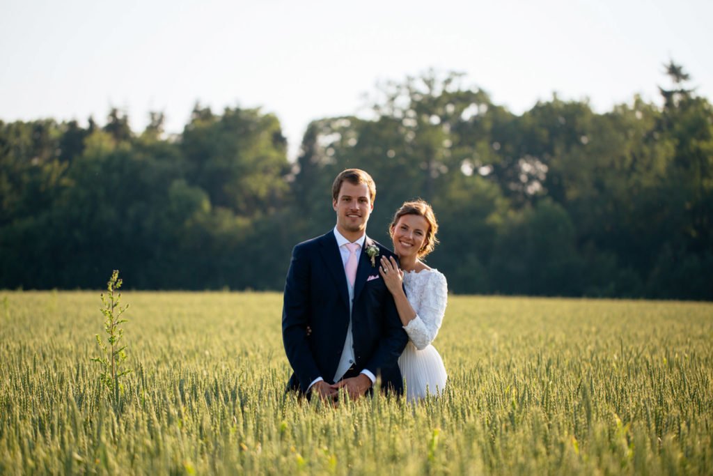 Deux mariés qui posent dans les champs en golden hour, par le photographe Maxime du Bus