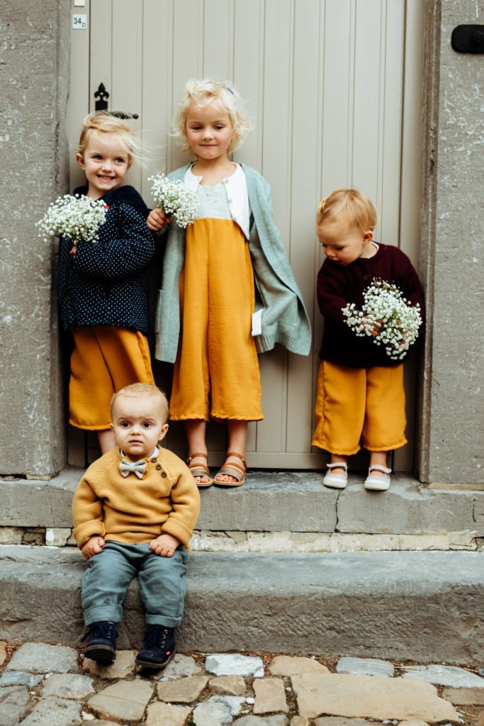 Des enfants bien habillés en jaune pour un mariage, qui posent devant une belle porte