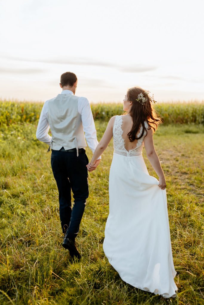 Deux mariés qui se tiennent par la main au soleil de fin de journée, lors de la golden hour